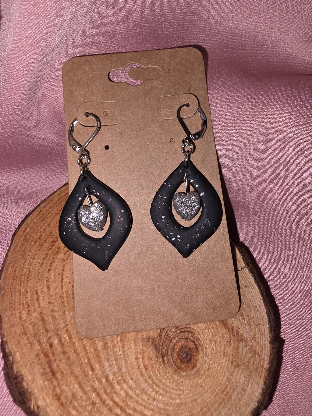 Handmade black clay open teardrop dangle earrings with silver glitter heart charm on silver leverback ear wires, on a kraft earring card