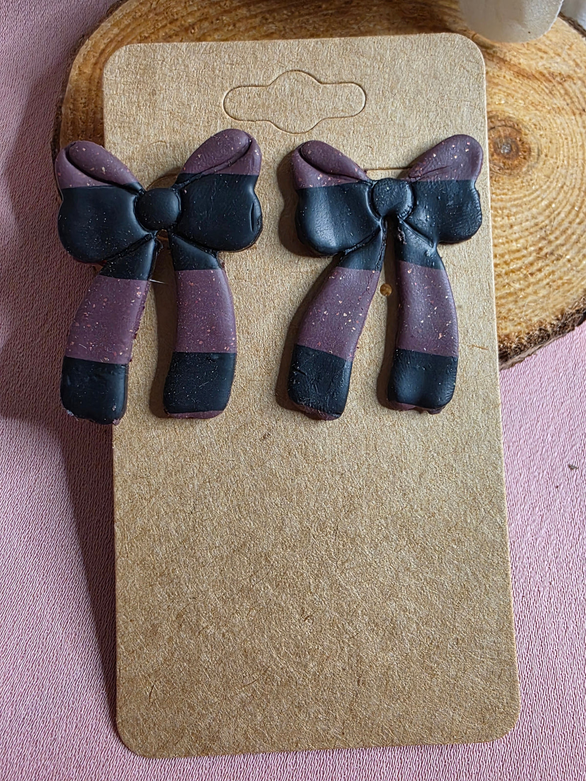 Close up detail of handmade dark purple and black color block clay bow stud earrings showing texture and color blocking on kraft earring card