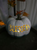 White and dusty blue carved pumpkin with BLESSED lettering glowing with warm candlelight
