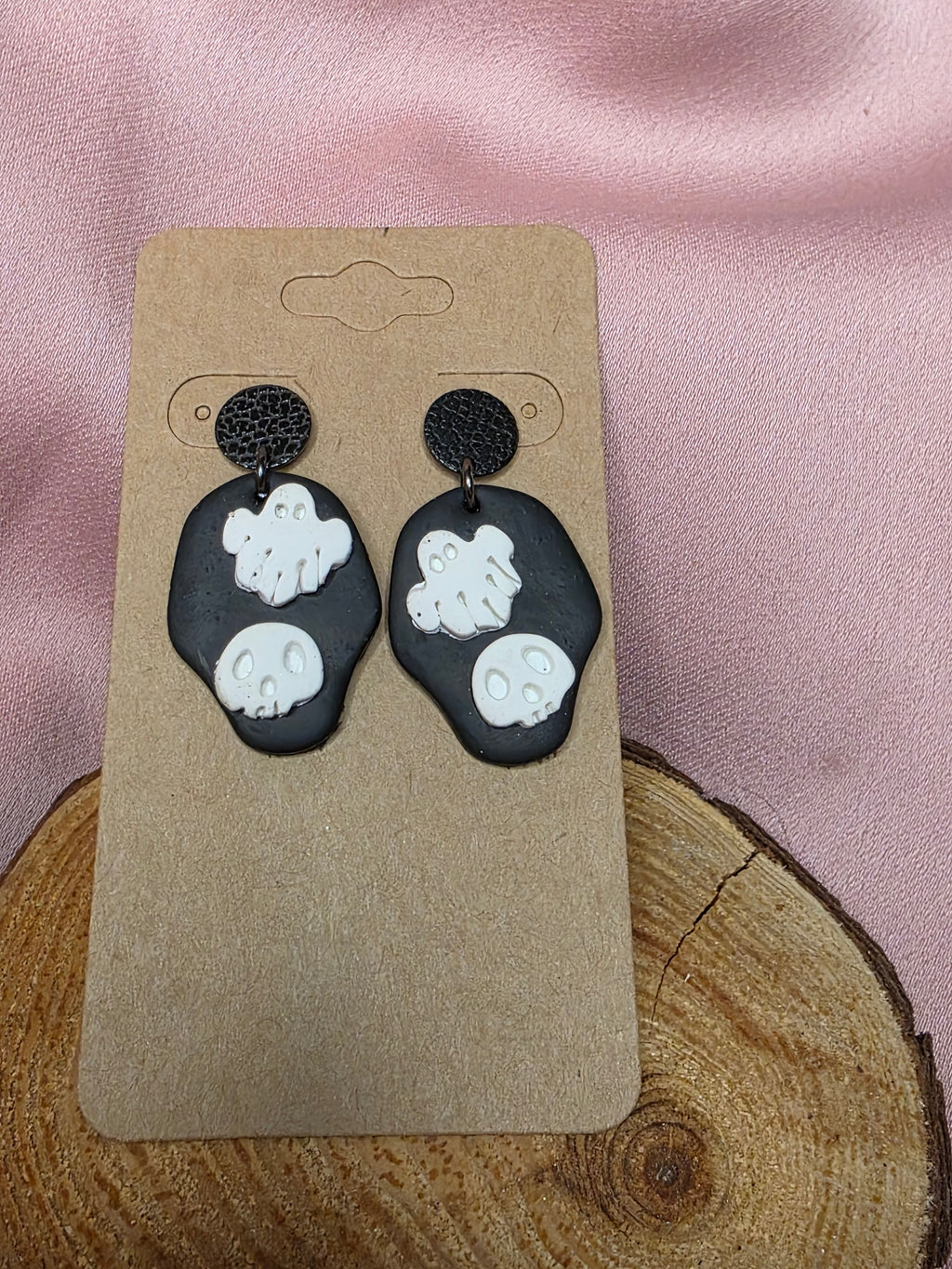 Handmade black clay dangle earrings with white ghost and skull appliqués on a kraft earring card