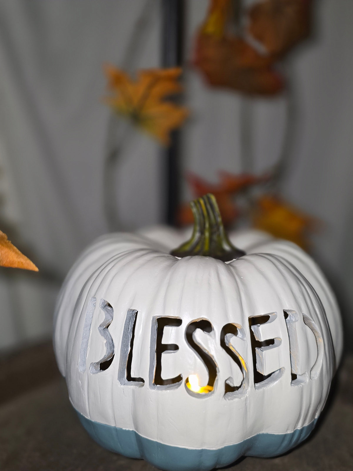 White and blue carved pumpkin with BLESSED lettering glowing with candlelight, close up view