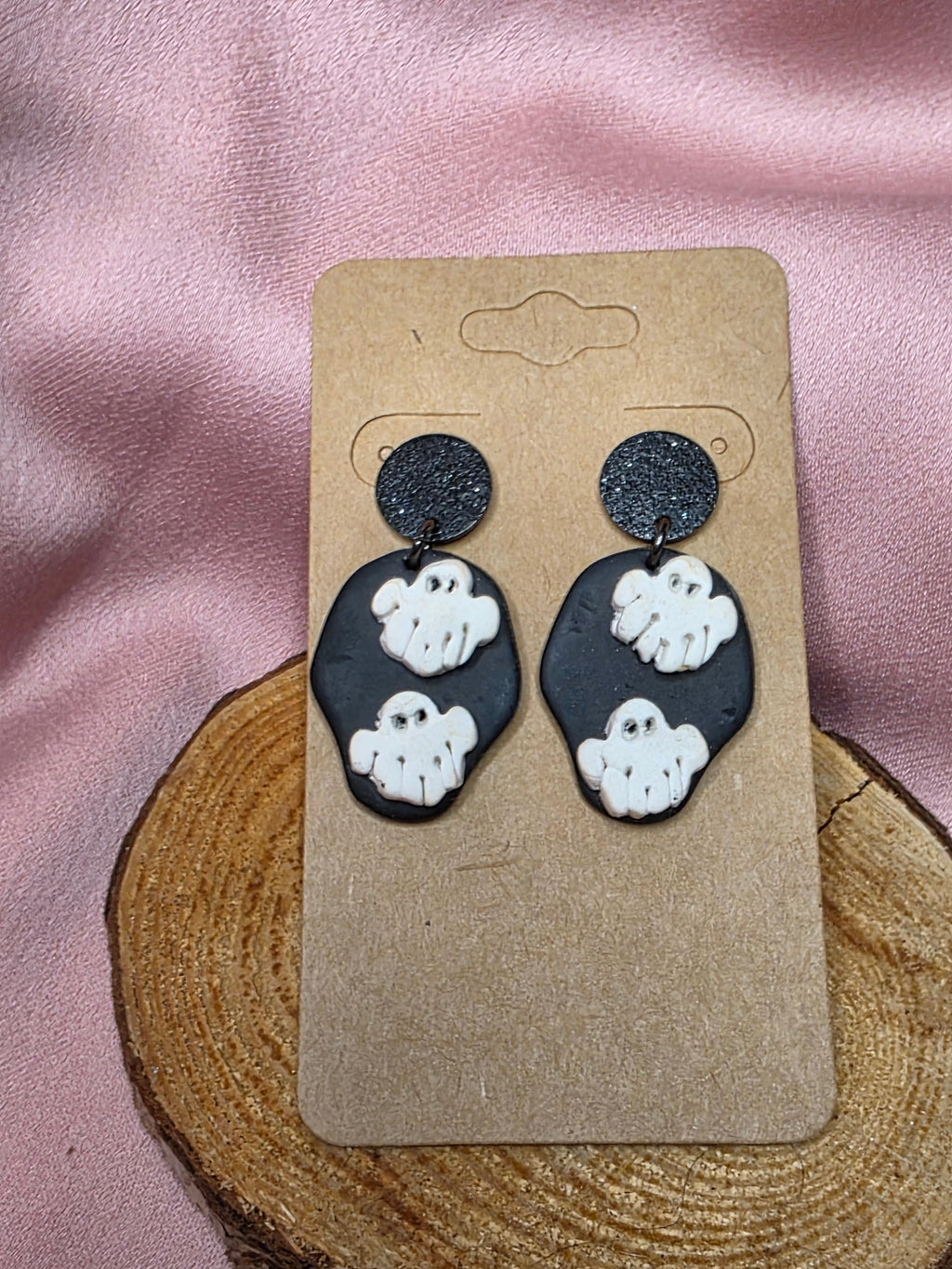 Handmade black clay dangle earrings with two white ghost appliqués on a kraft earring card