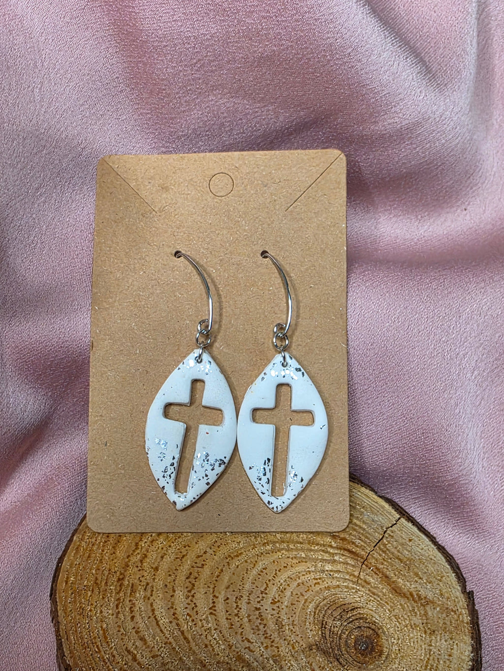 White cross cutout dangle earrings with silver-tone flecks on a display card