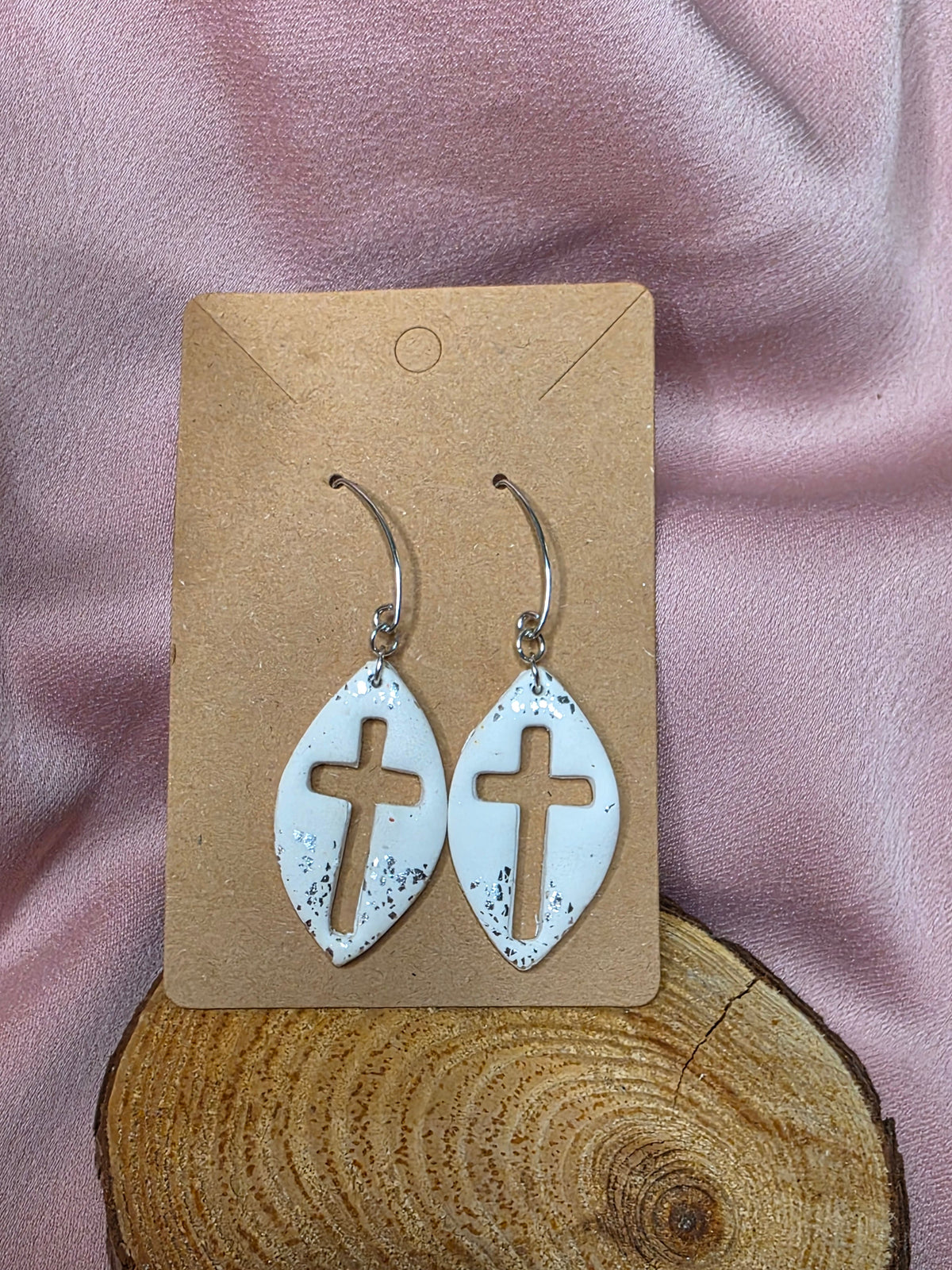 White cross cutout dangle earrings with silver-tone flecks on a display card