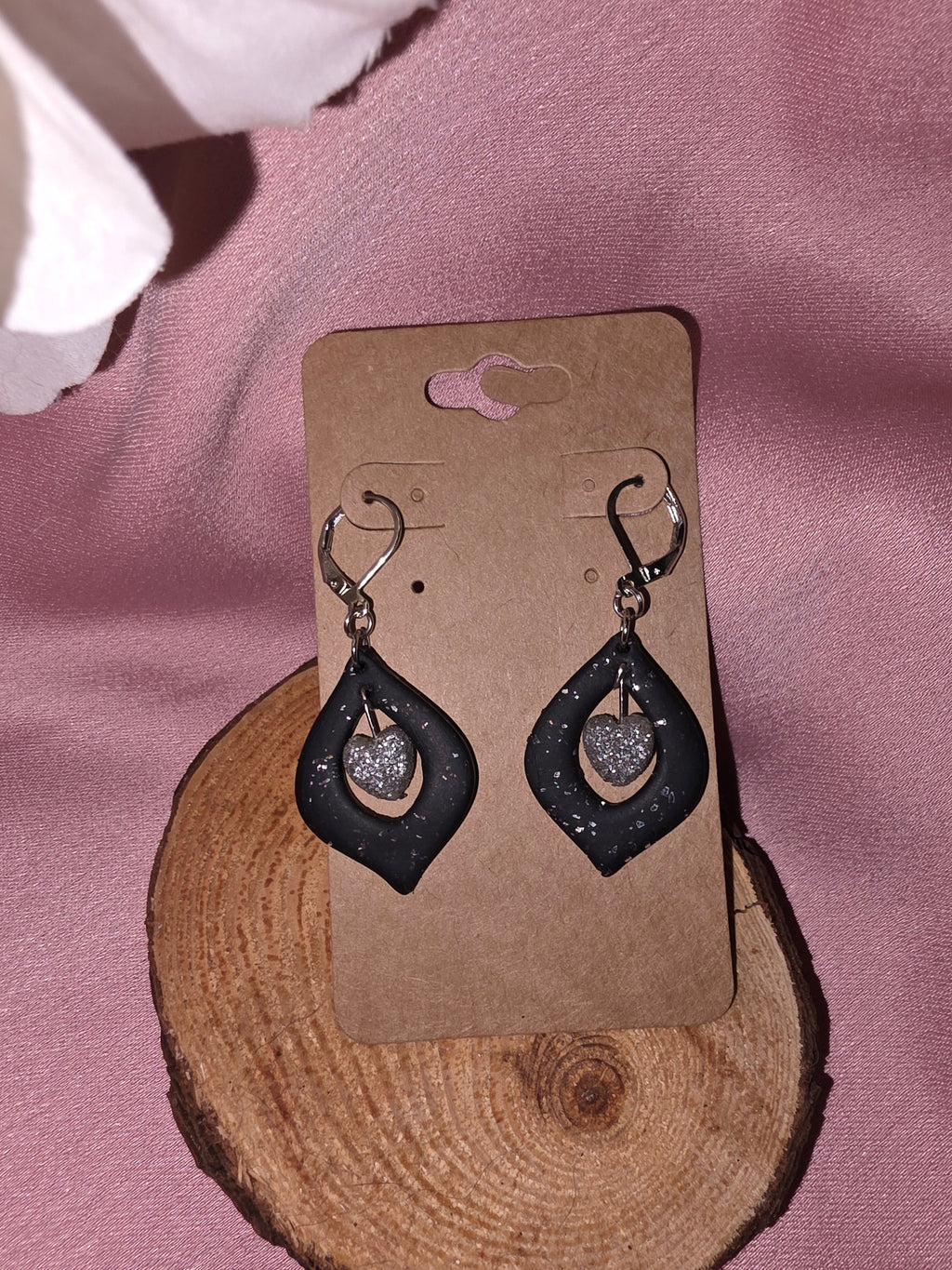 Handmade black clay open teardrop dangle earrings with silver glitter heart charm, close view on a kraft earring card